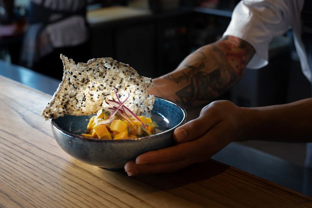 Plato de ceviche de mango y pescado con crujiente de arroz, siendo presentado por el chef durante un menú Omakase de Katagi Blau, en Mallorca.